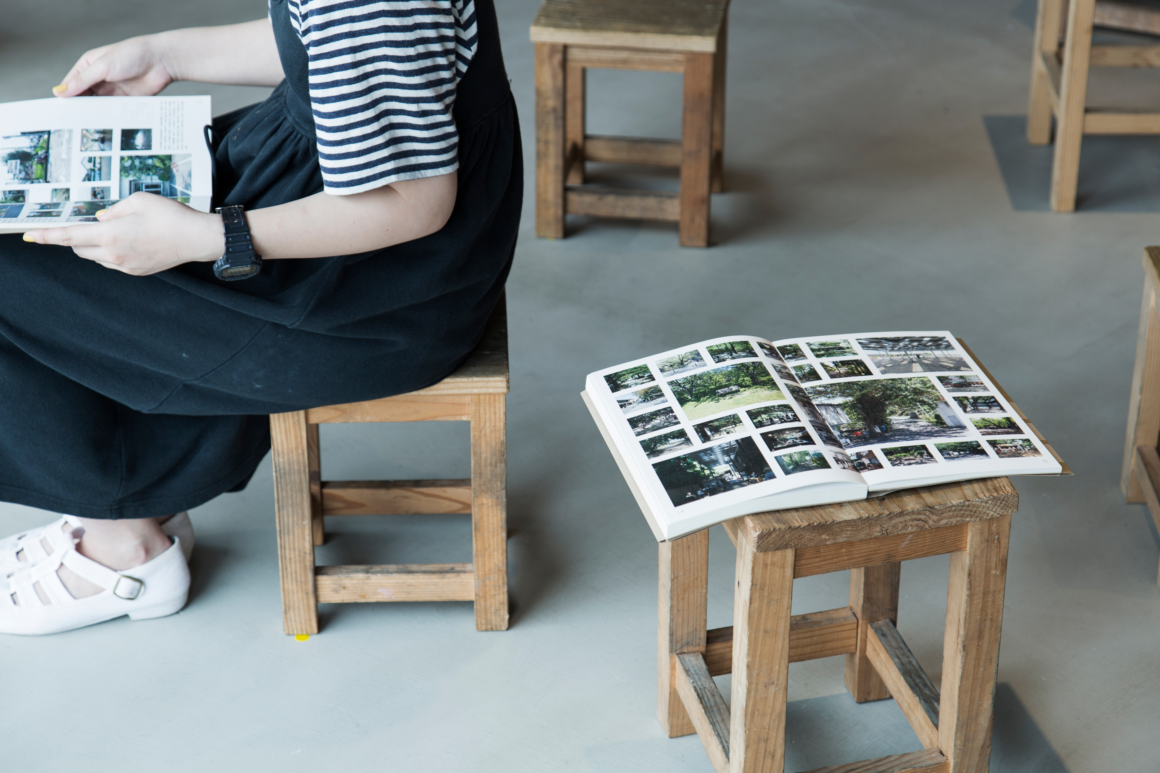 Open book of images on stool with person sitting next to it